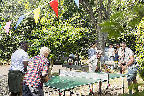 Männliche Freunde spielen Tischtennis im sonnigen Hinterhof