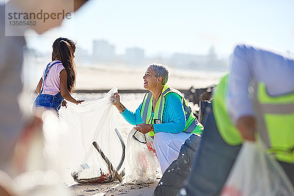 Ältere Frau und Mädchen beseitigen freiwillig Müll am sonnigen Strand