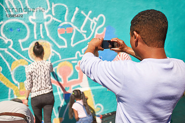 Mann mit Fotohandy fotografiert Wandgemälde der Gemeinde an einer sonnigen Wand