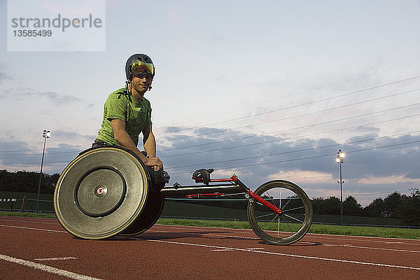 Porträt eines selbstbewussten jungen querschnittsgelähmten Sportlers  der auf einer Sportbahn für ein Rollstuhlrennen trainiert