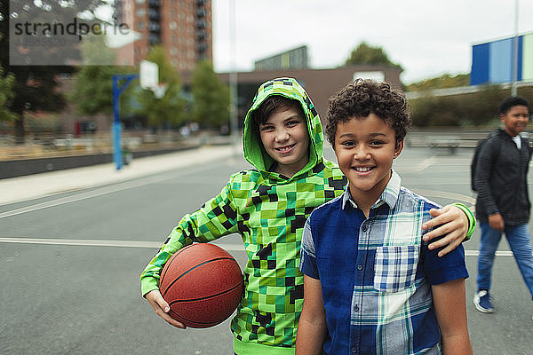 Porträt eines glücklichen Jungen in der Mittelstufe  der auf dem Schulhof Basketball spielt