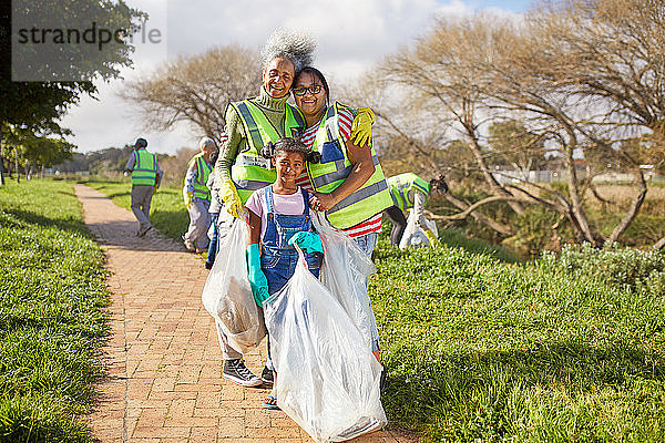 Porträt glücklicher Mehrgenerationen-Frauen  die ehrenamtlich Müll in einem sonnigen Park aufräumen