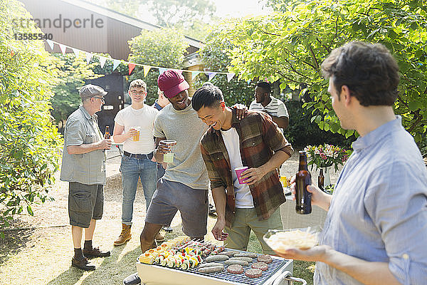 Männliche Freunde trinken Bier und grillen im sonnigen Sommergarten