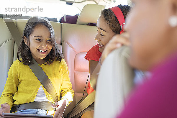 Glückliche Schwestern auf dem Rücksitz eines Autos mit digitalem Tablet