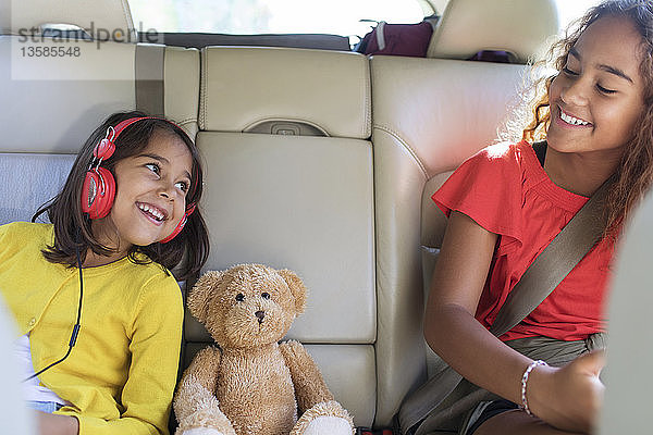 Glückliche Schwestern und Teddybär auf dem Rücksitz eines Autos