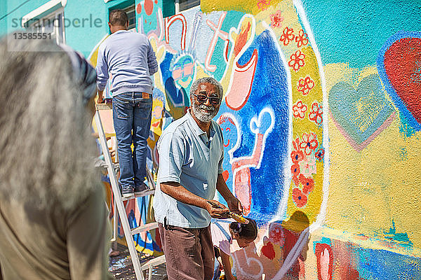 Älterer Mann malt als Freiwilliger ein lebendiges Wandgemälde an eine sonnige Wand