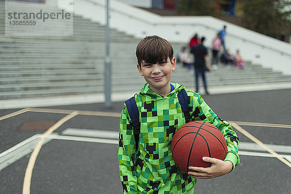Porträt eines selbstbewussten Jungen mit Basketball auf dem Schulhof
