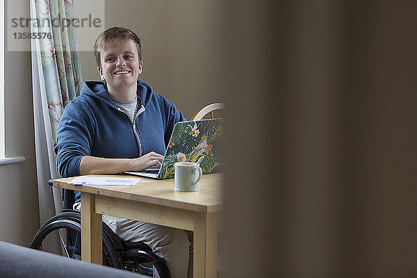 Porträt einer lächelnden  selbstbewussten jungen Frau im Rollstuhl am Laptop