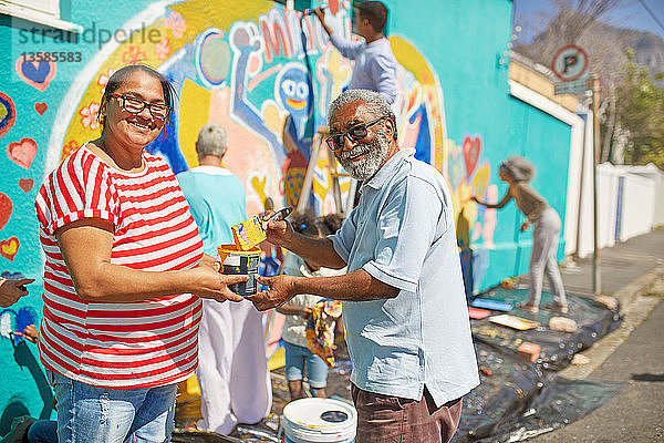 Porträt glücklicher Freiwilliger  die ein Wandbild auf einer sonnigen Stadtmauer malen