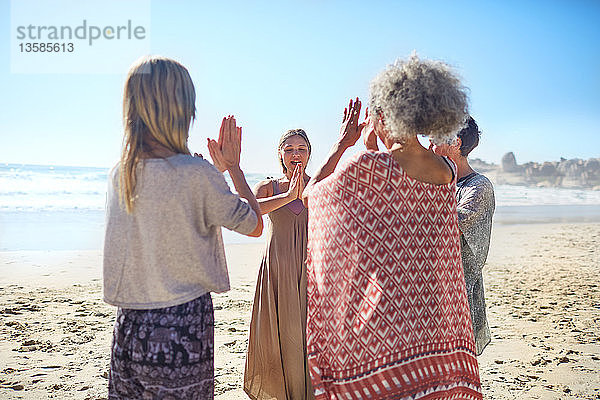 Freundinnen mit verschränkten Händen im Kreis am sonnigen Strand während eines Yoga-Retreats