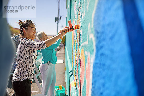 Frauen malen ein lebendiges Wandgemälde auf eine sonnige Stadtmauer