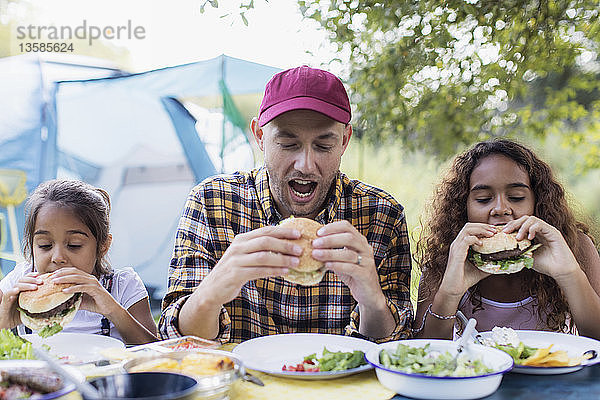 Vater und Töchter essen Grillhamburger auf dem Campingplatz
