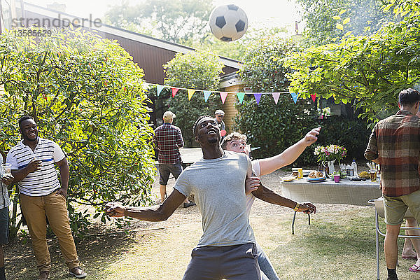 Männliche Freunde spielen Fußball und genießen ein sommerliches Grillfest im Hinterhof