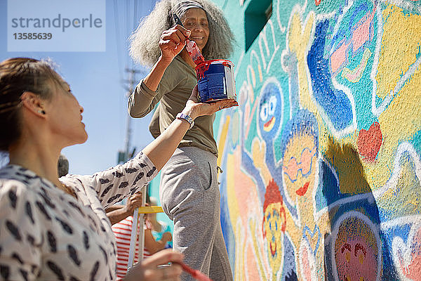 Freiwillige Frauen malen ein lebendiges Wandbild auf einer sonnigen Stadtmauer