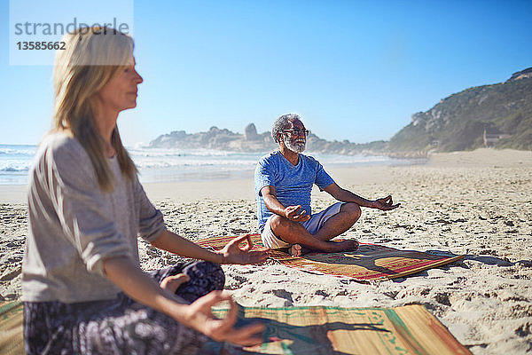 Gelassene Menschen meditieren am sonnigen Strand während eines Yoga-Retreats