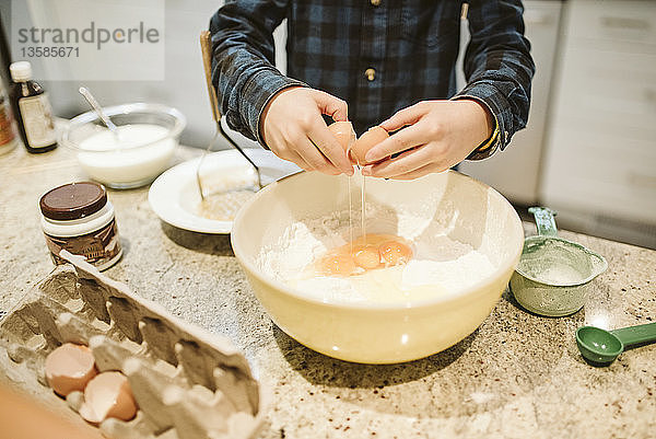 Junge beim Backen  der in der Küche ein Ei in eine Schüssel schlägt