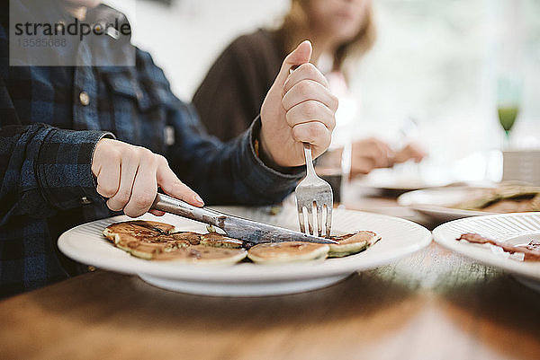 Nahaufnahme eines Jungen  der Pfannkuchen mit Gabel und Messer schneidet