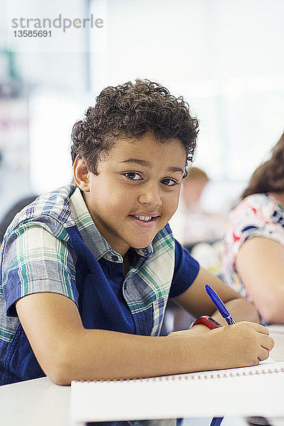 Porträt eines selbstbewussten Jungen im Grundschulalter  der im Klassenzimmer seine Hausaufgaben macht