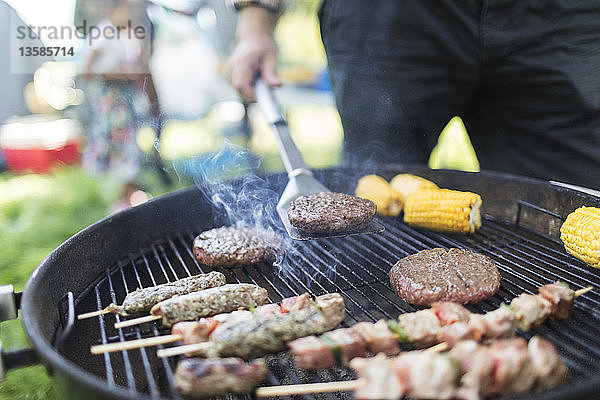 Mann beim Grillen von Hamburgern  Spießen und Maiskolben