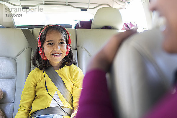 Lächelndes Mädchen mit Kopfhörern auf dem Rücksitz eines Autos