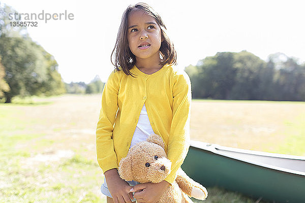 Mädchen mit Teddybär in sonnigem Feld mit Kanu