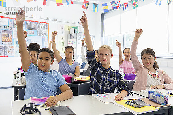 Eifrige Schüler der Junior High School mit erhobenen Händen im Klassenzimmer