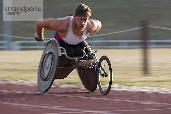 Entschlossener junger querschnittsgelähmter Sportler  der in einem Rollstuhlrennen über eine Sportstrecke rast