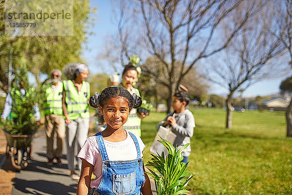 Porträt lächelndes  selbstbewusstes Mädchen  das freiwillig Bäume in einem sonnigen Park pflanzt