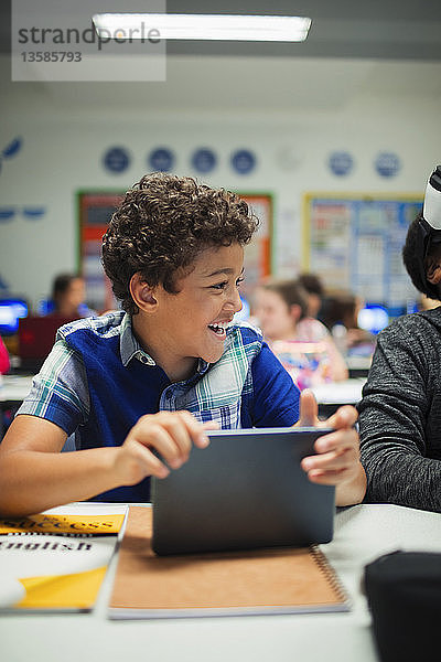 Glücklicher Grundschüler  der ein digitales Tablet im Klassenzimmer benutzt