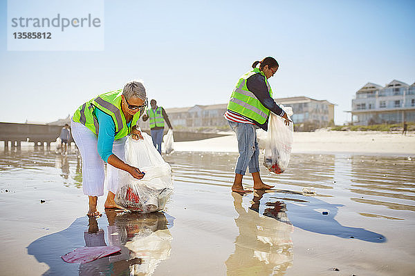 Weibliche Freiwillige sammeln Müll am sonnigen  nassen Sandstrand auf