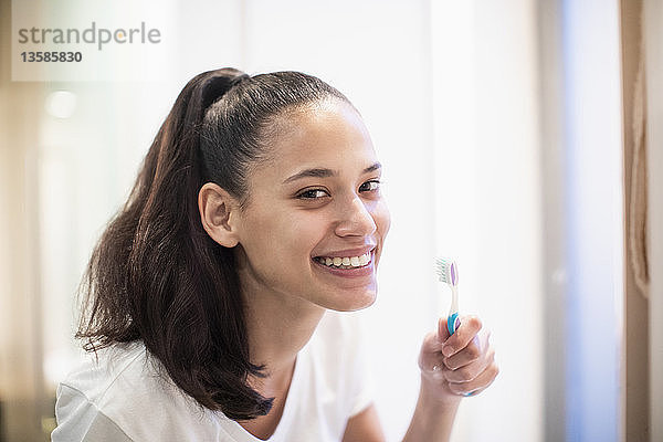 Porträt einer lächelnden  selbstbewussten Frau beim Zähneputzen im Badezimmerspiegel