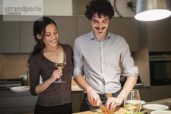 Glückliches Paar bei der Zubereitung des Abendessens und beim Trinken von Weißwein in der Wohnküche