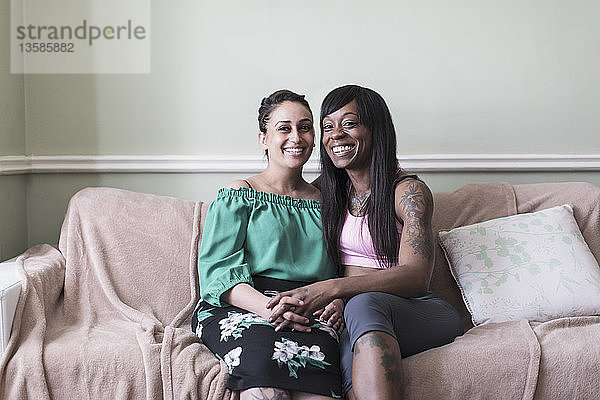 Porträt eines glücklichen  liebevollen lesbischen Paares  das sich auf dem Wohnzimmersofa an den Händen hält
