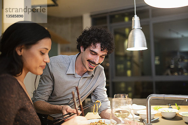 Lächelndes Paar isst Abendessen mit Stäbchen in der Wohnküche
