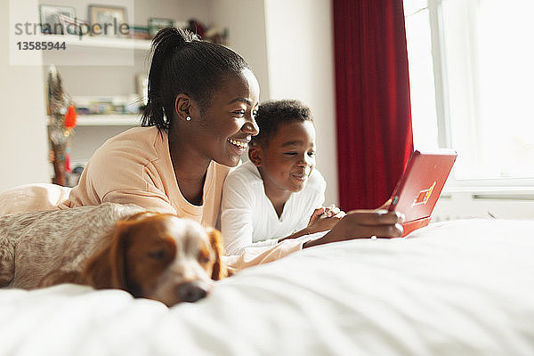 Mutter und Sohn benutzen digitales Tablet auf dem Bett neben dem schlafenden Hund