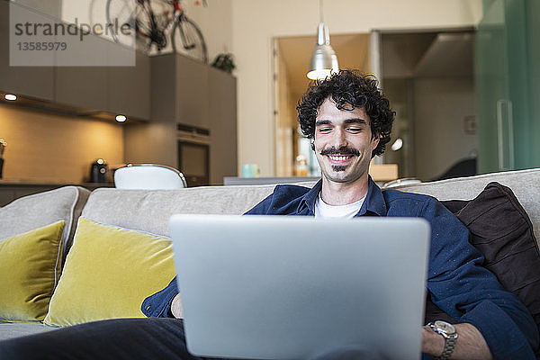 Lächelnder Mann mit Laptop auf dem Sofa einer Wohnung