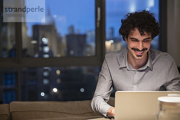 Mann benutzt nachts einen Laptop in einer städtischen Wohnung