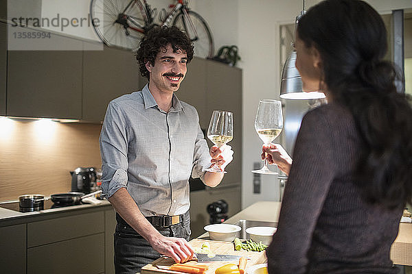 Ehepaar bereitet Abendessen vor und trinkt Weißwein in der Wohnküche