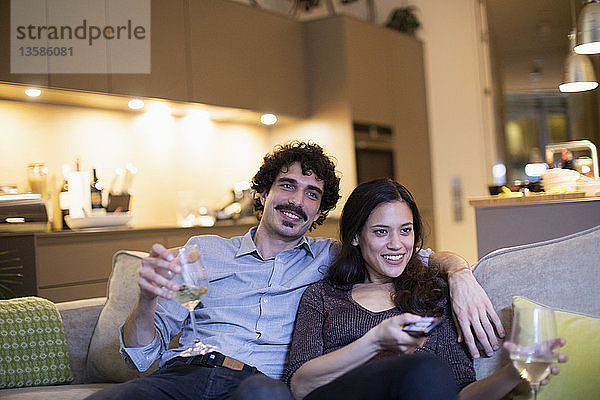 Glückliches Paar trinkt Weißwein und sieht auf dem Sofa fern
