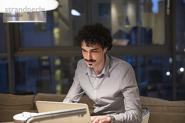 Konzentrierter Mann arbeitet nachts am Laptop in einer städtischen Wohnung