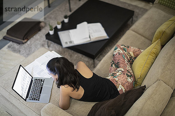Frau im Schlafanzug arbeitet am Laptop auf dem Wohnzimmersofa