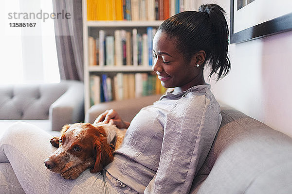 Junge Frau kuschelt mit Hund auf Wohnzimmersofa
