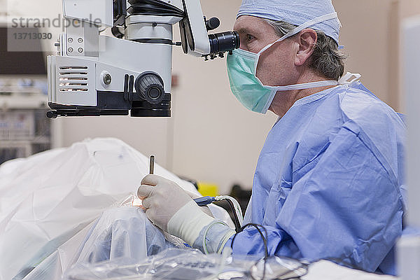 Arzt schaut in ein Mikroskop und benutzt ein Cracker-Instrument und ein Phako-Handstück während einer Kataraktoperation