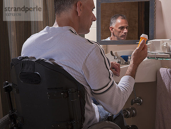 Mann mit Rückenmarksverletzung im Rollstuhl schaut auf eine Pillenflasche
