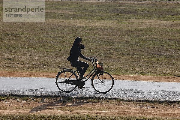 Eine kambodschanische Frau fährt mit dem Fahrrad auf einer kleinen Straße  Siem Reap  Kambodscha.