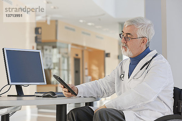 Arzt mit Muskeldystrophie im Rollstuhl schaut auf sein Tablet