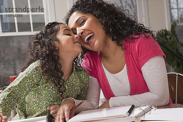 Hispanische Frau  die mit ihrer Tochter lacht  während sie Hausaufgaben macht