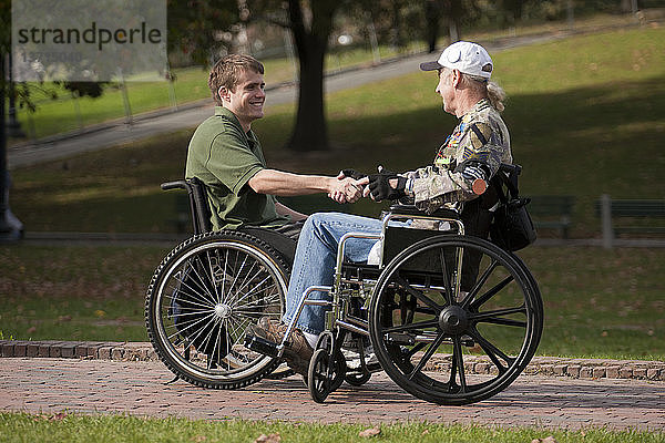 Zwei Veteranen schütteln sich in Rollstühlen die Hände