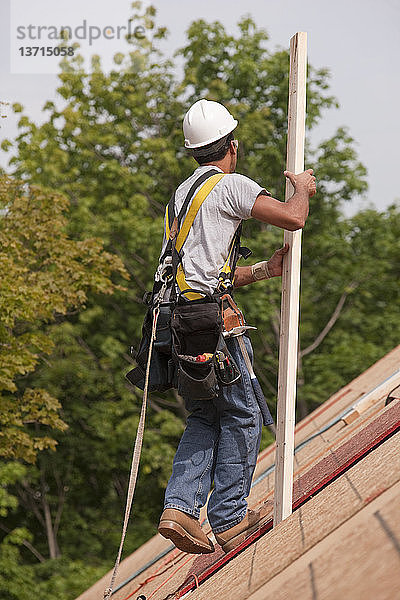 Spanischer Zimmermann trägt Bretter auf dem Dach eines im Bau befindlichen Hauses