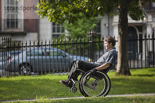 Mann mit Querschnittslähmung im Rollstuhl auf einem Weg in einem öffentlichen Park